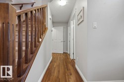 Hardwood-finish flooring extending through a hallway with white paneled doors, light grey wall paint, and white trim - 