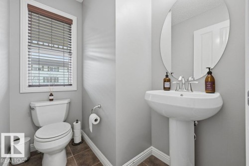 Pedestal sink with an oval mirror and a chrome faucet, featuring light gray walls, white trim, and wood-finish flooring - 1613 Kerr Road, Edmonton, AB - Indoor Photo Showing Bathroom