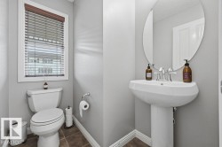 Pedestal sink with an oval mirror and a chrome faucet, featuring light gray walls, white trim, and wood-finish flooring - 