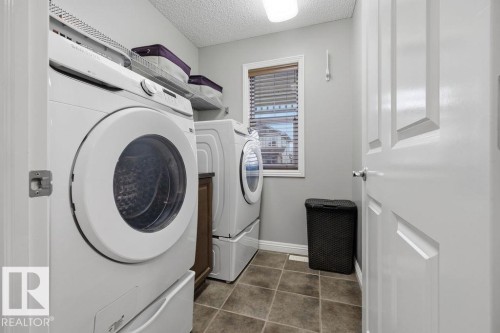 Dedicated laundry area featuring dual front-load appliances, tiled flooring, and a window with blinds - 1613 Kerr Road, Edmonton, AB - Indoor Photo Showing Laundry Room