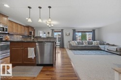 Open-concept living space featuring a kitchen with wood cabinetry, stainless steel appliances, and a tiled backsplash - 