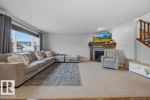 Carpeted living area featuring a prominent window, a fireplace with a wood mantle, and a staircase with wood railing - 1613 Kerr Road, Edmonton, AB - Indoor Photo Showing Living Room With Fireplace