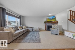 Carpeted living area featuring a prominent window, a fireplace with a wood mantle, and a staircase with wood railing - 