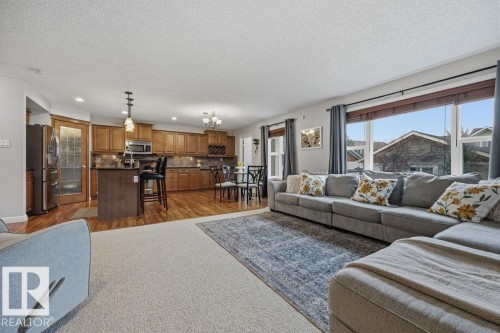 Open-concept living space featuring wood-finish flooring, a kitchen island with pendant lighting, stainless steel appliances, and large windows - 1613 Kerr Road, Edmonton, AB - Indoor Photo Showing Living Room