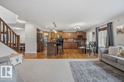 Open-concept kitchen and living area featuring wood-finish flooring, stainless steel appliances, and a central island with seating - 