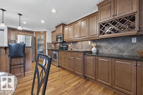Kitchen featuring wood-finish flooring, dark stone countertops, tile backsplash, stainless steel appliances, and a built-in wine rack - 1613 Kerr Road, Edmonton, AB - Indoor Photo Showing Kitchen