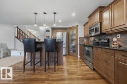Kitchen featuring wood-finish flooring, two-tone cabinetry, stainless steel appliances, a breakfast bar with pendant lighting, and a pantry with a frosted glass door - 