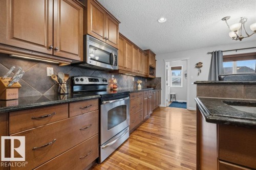 Kitchen featuring wood-finish cabinetry, dark countertops, stainless steel appliances, and wood-finish flooring - 1613 Kerr Road, Edmonton, AB - Indoor Photo Showing Kitchen