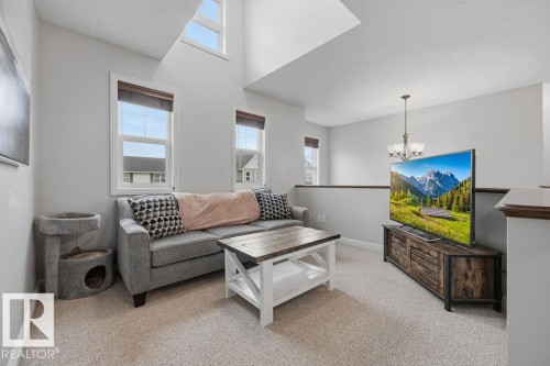 2nd floor bonus room >Loft area featuring high ceilings, upper and lower windows, carpet flooring, a wood-finish media console, and a contemporary chandelier - 1613 Kerr Road, Edmonton, AB - Indoor Photo Showing Living Room