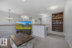 Carpeted landing featuring a built-in wood bookshelf, a wood-finish handrail, and a contemporary chandelier - 