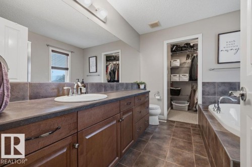 Bathroom featuring a single vanity with wood cabinetry, a large mirror, a built-in tub with tile surround, an open closet, and tile flooring - 1613 Kerr Road, Edmonton, AB - Indoor Photo Showing Bathroom