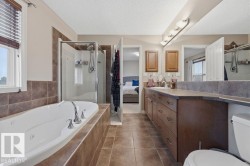 Bathroom featuring a built-in jetted tub with tile surround, a glass-enclosed shower, a double vanity with ample storage, and tiled flooring - 