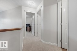 Carpeted hallway featuring a wood-finish handrail, white trim, and interior doors - 
