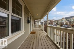 Spacious covered front porch with wood-finish decking and white baluster railing - 
