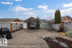 Spacious paved patio area featuring a detached garage with exterior siding, a privacy fence, and a built-in stone fire pit with surrounding seating - 