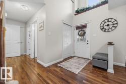 Spacious entry featuring wood-finish flooring, a white paneled front door with decorative glass, and a high ceiling - 