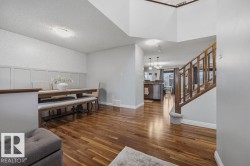 Rich wood-finish flooring extends through the main level, featuring a dining area with decorative wainscoting and a staircase with wood balusters - 