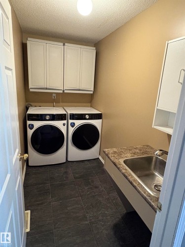 Laundry area featuring white cabinetry, a built-in stainless steel sink, and dark tiled flooring - 5306 44 Street, Cold Lake, AB - Indoor Photo Showing Laundry Room