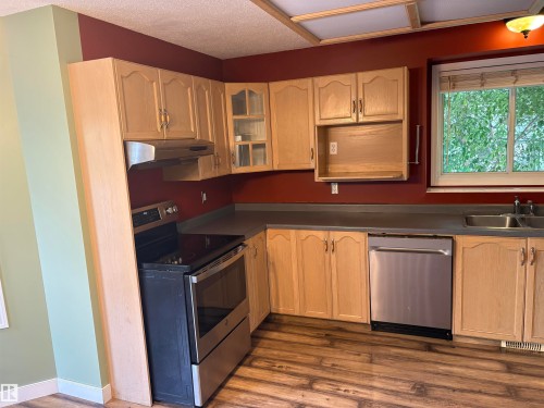 Kitchen featuring wood-finish flooring, light wood cabinetry, stainless steel range, stainless steel dishwasher, and a double basin sink - 5306 44 Street, Cold Lake, AB - Indoor Photo Showing Kitchen With Double Sink