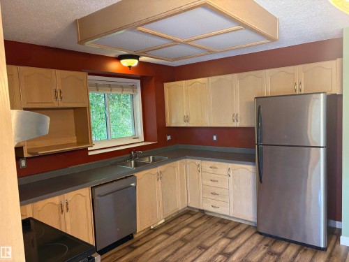 Wood-finish flooring with light wood cabinetry, dark countertops, and stainless-steel appliances - 5306 44 Street, Cold Lake, AB - Indoor Photo Showing Kitchen With Double Sink