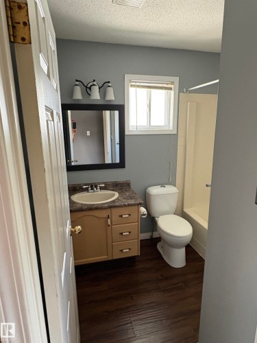 Vanity with an integrated sink, wood-finish flooring, full bathtub with shower, and a framed mirror - 5306 44 Street, Cold Lake, AB - Indoor Photo Showing Bathroom
