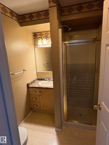 Bathroom featuring a vanity with a composite countertop and integrated sink, a built-in mirror, a two-light fixture, and a shower enclosure with glass doors - 5306 44 Street, Cold Lake, AB - Indoor Photo Showing Bathroom