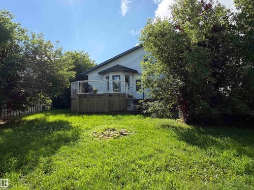 Rear exterior featuring a wood-decked patio with glass panel railing, white siding, and a gabled roofline - 5306 44 Street, Cold Lake, AB - Outdoor