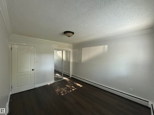 Spacious room featuring wood-finish flooring, white walls, and crown molding - 111 10225 117 Street, Edmonton, AB 