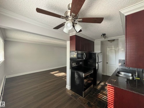 Open-concept kitchen featuring dark wood-finish cabinetry, stainless steel appliances, and a double basin sink with a modern faucet - 111 10225 117 Street, Edmonton, AB 