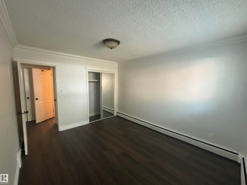 Room featuring wood-finish flooring, white painted walls, and white crown molding - 111 10225 117 Street, Edmonton, AB 