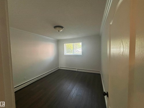 Room featuring dark wood-finish flooring, crisp white walls, and a single window with blinds - 111 10225 117 Street, Edmonton, AB 
