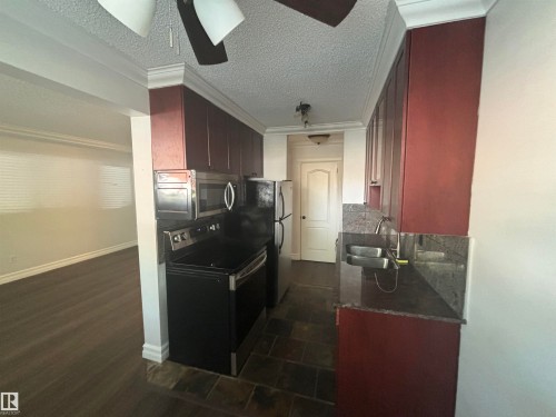 Galley kitchen featuring dark wood-finish cabinetry, stainless steel appliances, and stone countertops - 111 10225 117 Street, Edmonton, AB 
