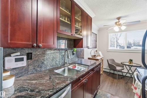 Kitchen featuring dark wood cabinetry, a stainless steel sink with a gooseneck faucet, and granite countertops - 111 10225 117 Street, Edmonton, AB 
