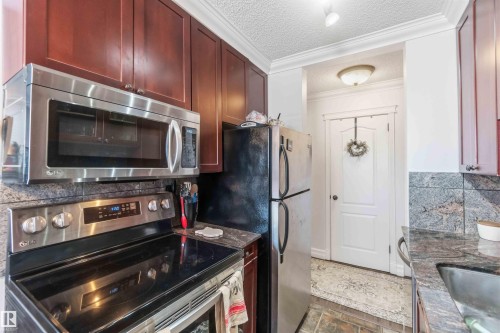 The kitchen features dark wood cabinetry, a stainless steel microwave, and a black and stainless steel electric range - 111 10225 117 Street, Edmonton, AB 