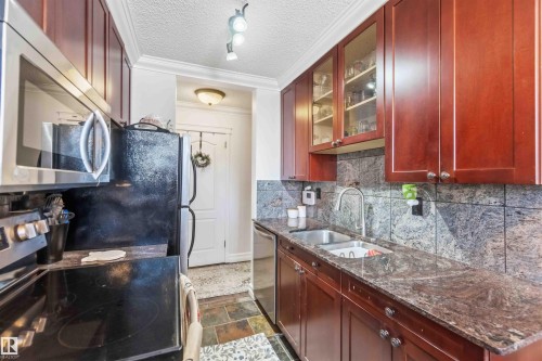 Kitchen featuring dark wood cabinetry, granite countertops, a stainless steel sink with a gooseneck faucet, and a tile backsplash - 111 10225 117 Street, Edmonton, AB 