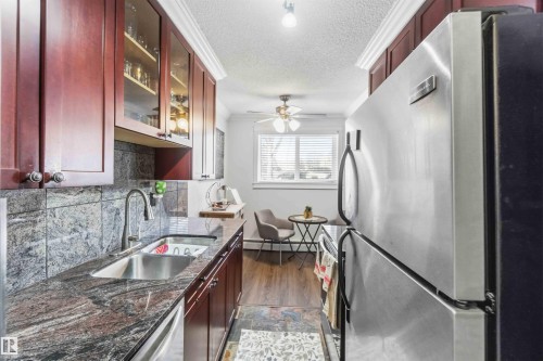The kitchen features dark wood cabinetry, a stainless steel sink with a goose-neck faucet, and granite countertops - 111 10225 117 Street, Edmonton, AB 