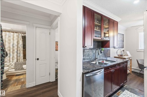Kitchenette featuring dark wood cabinetry, a stainless steel sink, a dishwasher, and granite countertops - 111 10225 117 Street, Edmonton, AB 