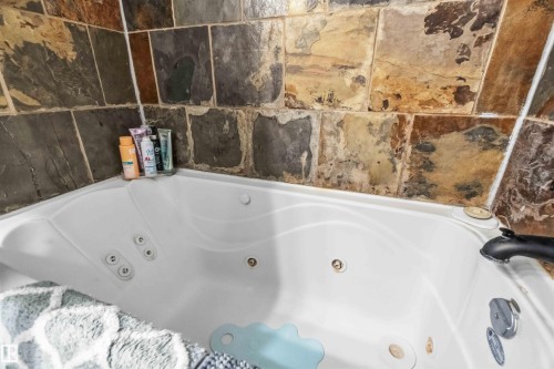 The property features a jetted bathtub with natural stone tile surround and a black faucet - 111 10225 117 Street, Edmonton, AB 