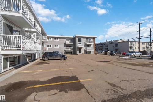 The property features a parking area with painted lines, and a multi-level building with balconies and white railings - 111 10225 117 Street, Edmonton, AB 