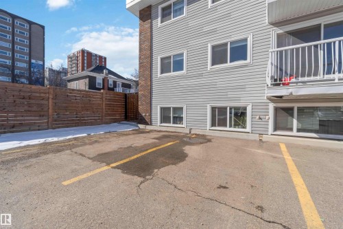 The property features a private parking area with painted lines, a wooden fence, and a gray exterior with white-framed windows - 111 10225 117 Street, Edmonton, AB 