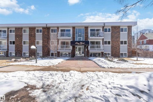 The property features a brick and siding exterior, multiple balconies with white railings, and a central entrance with a canopy - 111 10225 117 Street, Edmonton, AB 