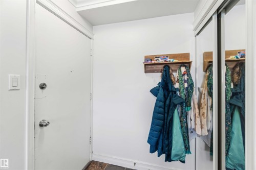 Entryway featuring a white door, light-colored walls, and mirrored closet doors - 111 10225 117 Street, Edmonton, AB 