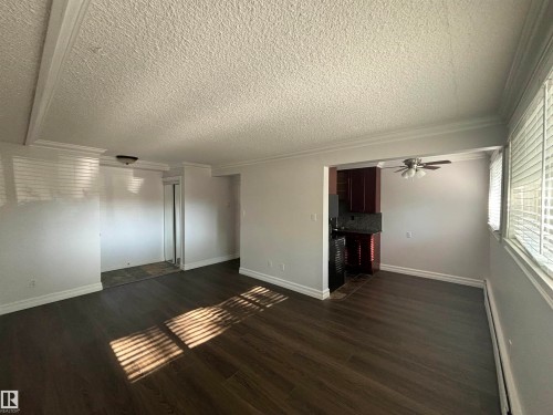 Spacious living area featuring wood-finish flooring, white baseboards, and crown molding - 111 10225 117 Street, Edmonton, AB 