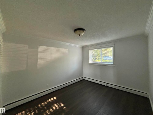 Room featuring dark wood-finish flooring, white walls, and crown molding - 111 10225 117 Street, Edmonton, AB 
