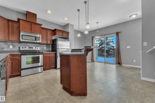 Kitchen featuring wood cabinetry, stainless steel appliances, and a central island with an extended counter - 110 13825 155, Edmonton, AB - Indoor Photo Showing Kitchen With Stainless Steel Kitchen
