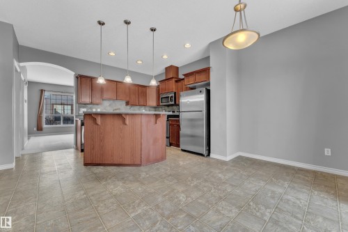 Kitchen featuring wood-finish cabinetry, stainless steel appliances, a tiled backsplash, and an island with pendant lighting - 110 13825 155, Edmonton, AB - Indoor Photo Showing Kitchen