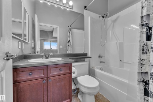 Bathroom featuring a dark wood-finish vanity with an integrated sink and dark countertop, a white toilet, and a white shower-over-tub combination with a chrome fixture - 110 13825 155, Edmonton, AB - Indoor Photo Showing Bathroom