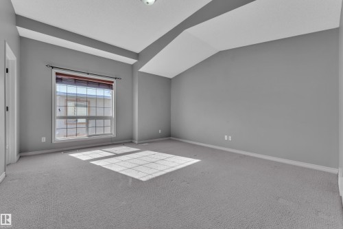 Spacious room featuring vaulted ceilings, a large multi-pane window with wood-finish blinds, light gray carpeting, and neutral gray walls - 110 13825 155, Edmonton, AB - Indoor Photo Showing Other Room