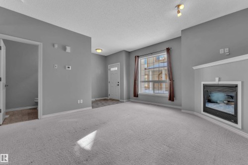 Living area with a built-in fireplace, a large window, light gray carpet, and a white front entry door - 110 13825 155, Edmonton, AB - Indoor With Fireplace