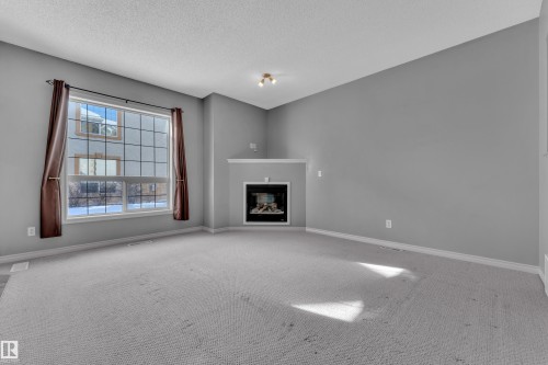 Spacious room featuring a corner fireplace with a white mantel, a large grid-pattern window, light-colored carpet flooring, and vaulted ceilings - 110 13825 155, Edmonton, AB - Indoor With Fireplace